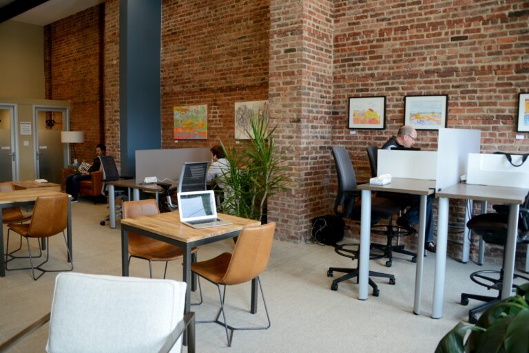 A room with brick walls. A laptop on top of a table with two chairs. People working.